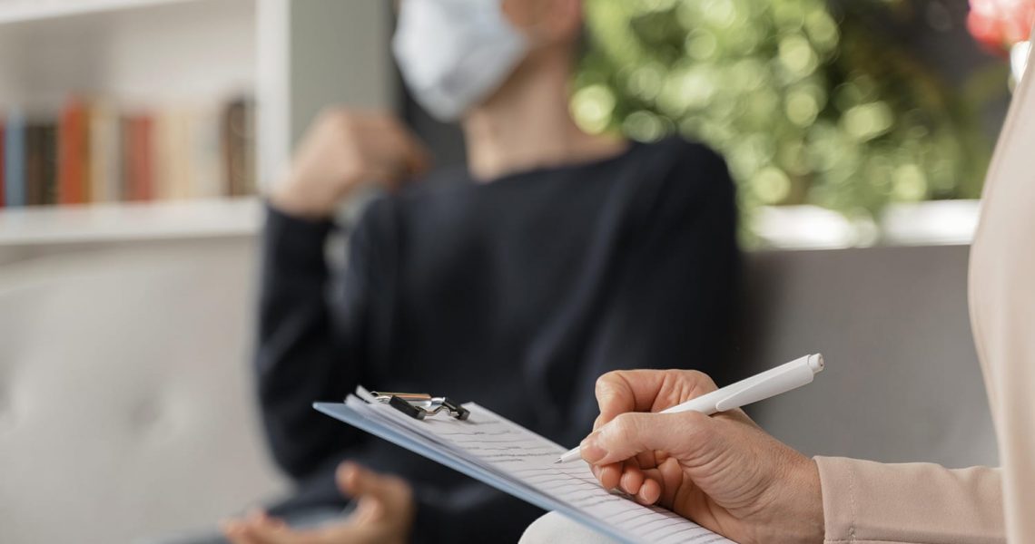 woman-therapist-taking-notes-man-therapy-office-with-mask